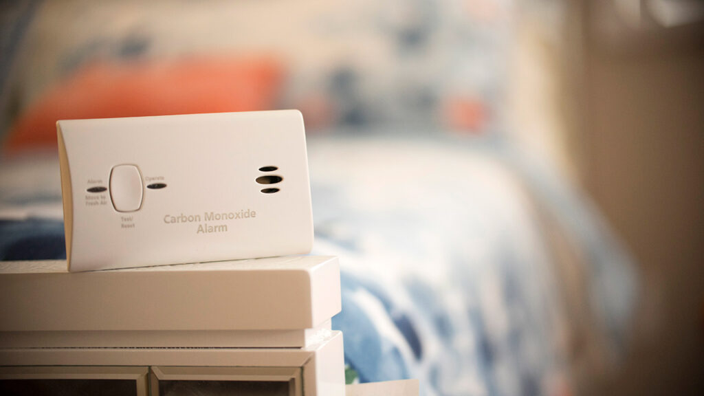 A white carbon monoxide alarm placed on the side of a bed.